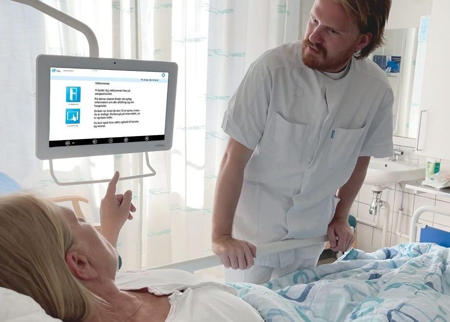 Sygeplejerske viser FlexCare-skærmen til en patient i sengen