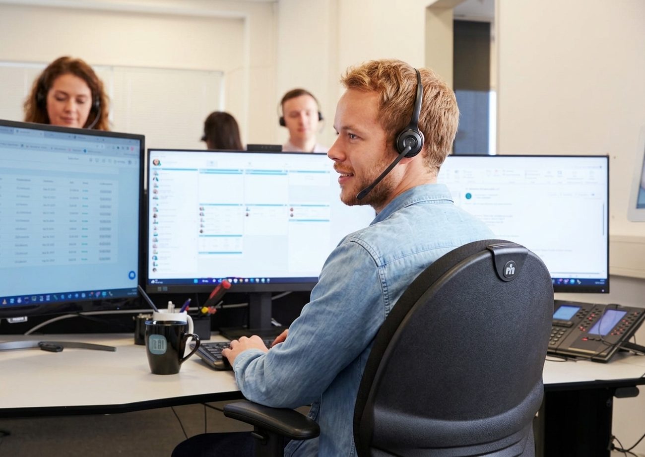 PowerNet-supporttekniker med headset ved to skærme midt i en supportopgave